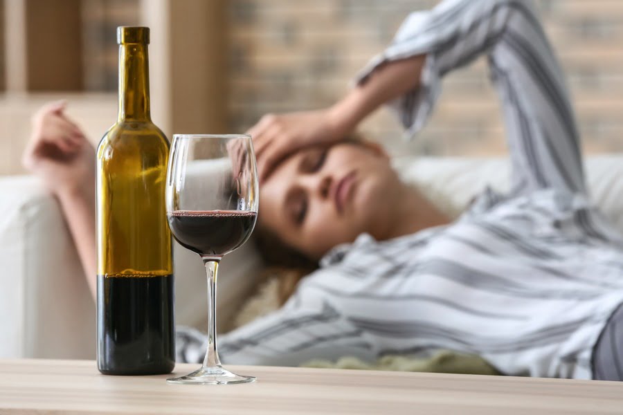 a woman lying on a couch while looking at a glass of red wine