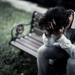 person sitting on a bench outdoors with their head in their hands