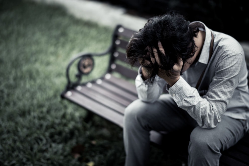 person sitting on a bench outdoors with their head in their hands