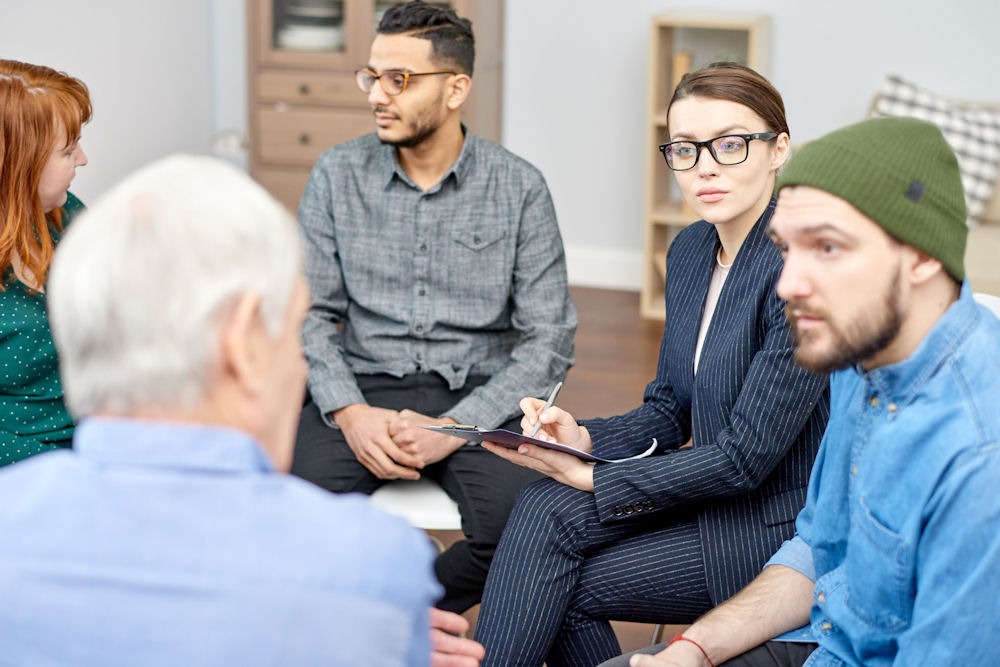 group of adults sitting in chairs and having discussion in group therapy