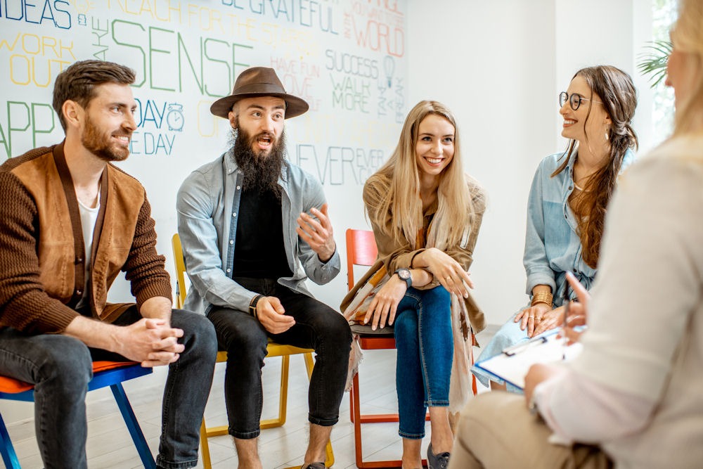 group of happy people sitting in circle of chairs