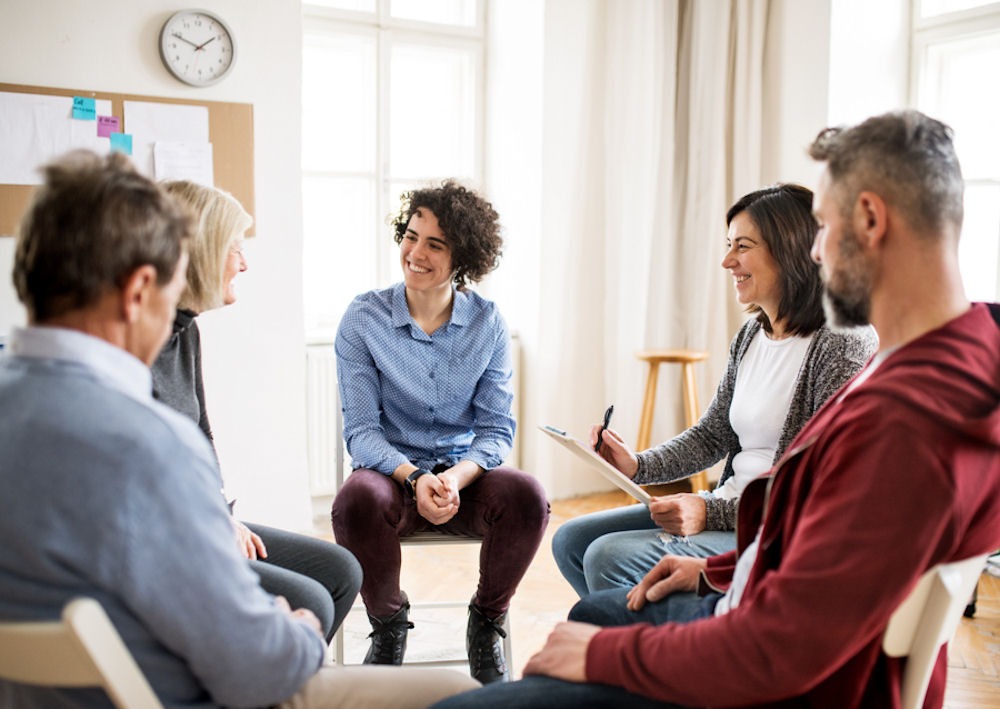 small support group meeting where adults are sitting in a circle smiling