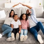 family sitting on the floor with parents putting their hands together over top like a house