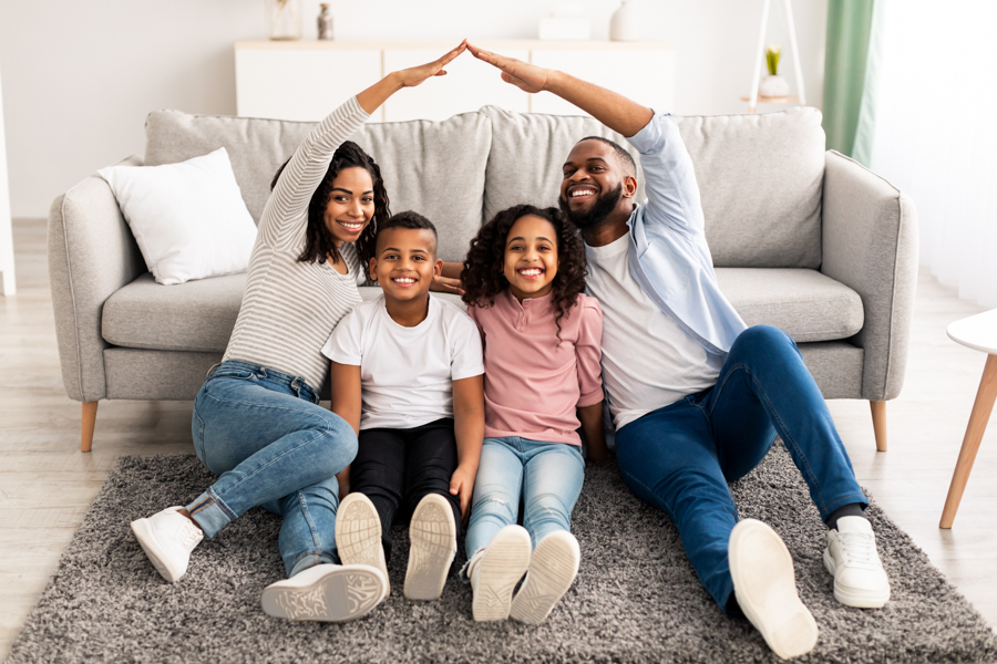 family sitting on the floor with parents putting their hands together over top like a house