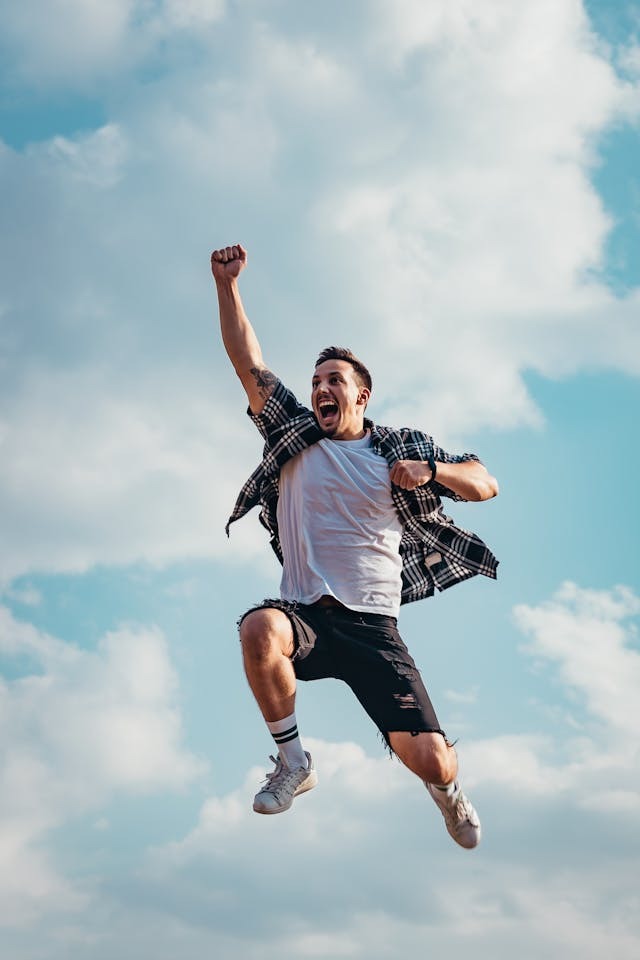 a man jumping with one hand raised and has clouds in background