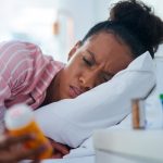 woman laying in bed looking at prescription bottle