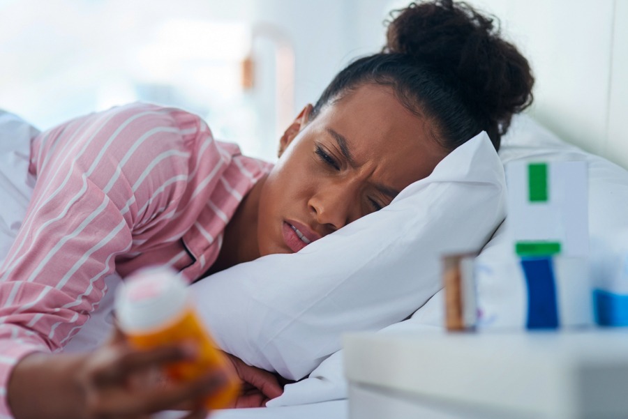 woman laying in bed looking at prescription bottle