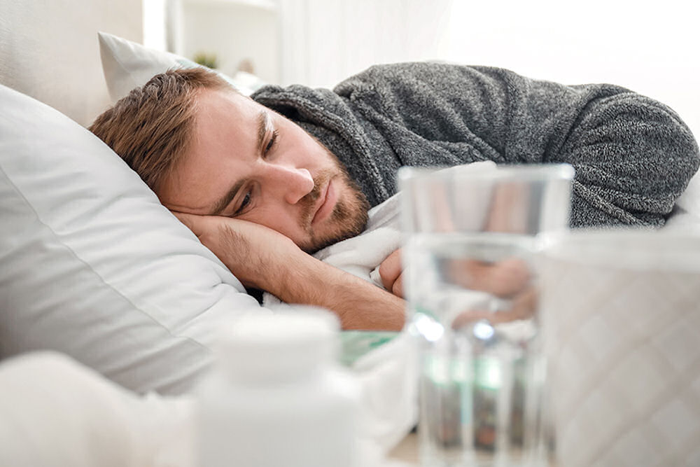 tired man laying in bed with a cup of water on a nightstand