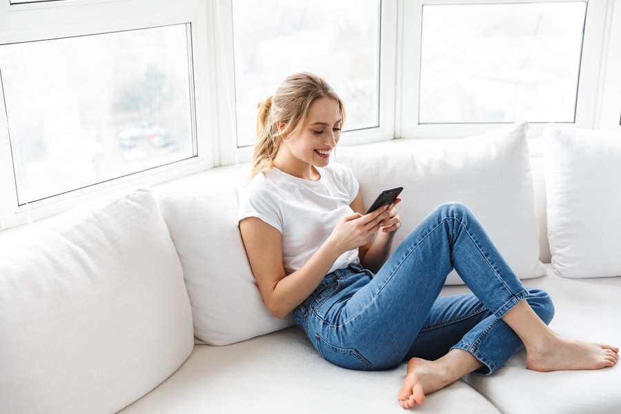 woman sitting on a white couch using her phone