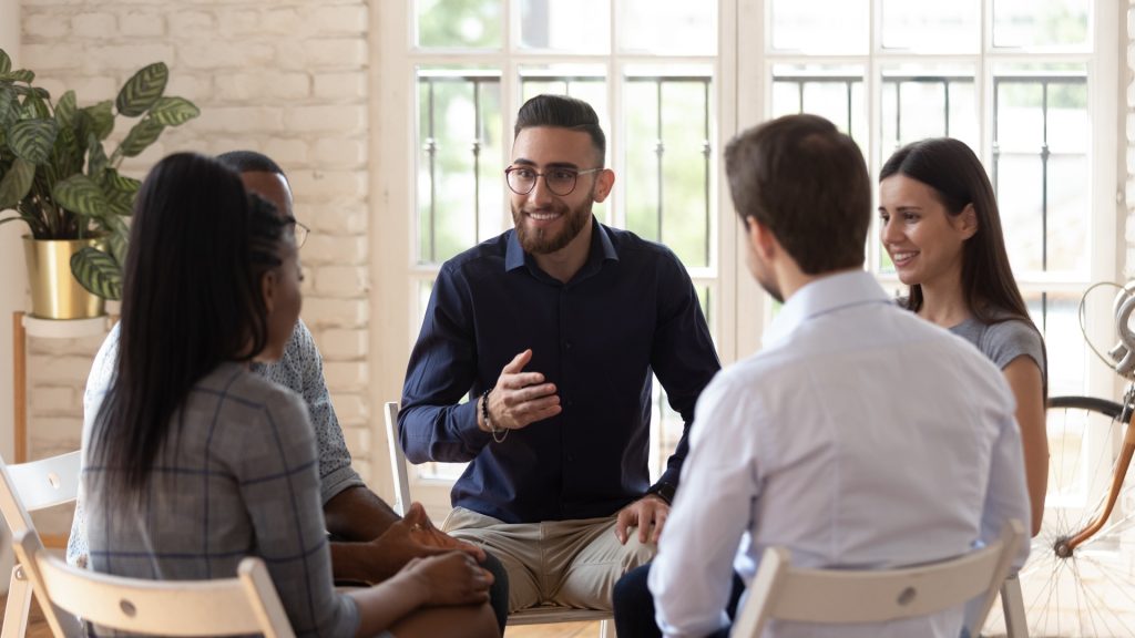 man in blue sweater addressing a small group in therapy