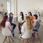 young adults sitting in circle of chairs