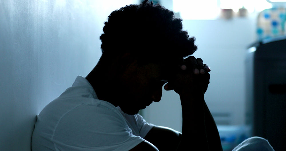 upset man sitting against a wall with head in hands