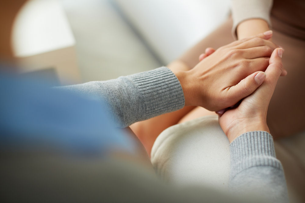 woman holding another's hand to comfort them